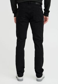 Svarta denimjeans med slim fit, fem fickor, platt midjeband och subtila sömdetaljer. Bärs med låga vita sneakers.