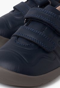 Scarpe di pelle blu navy con un design testurizzato, dotate di due cinturini regolabili in velcro e una suola in gomma grigia, che garantiscono una calzata sicura e comfort.