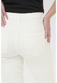 Pantalons en denim blanc au design ajusté, comportant deux poches arrière et une texture lisse. La taille est mi-haute avec passants de ceinture.
