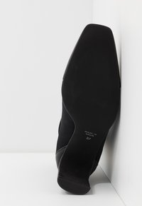 Botte chevillère en daim noir avec un bout pointu et un design épuré. La semelle est plate, avec une texture antidérapante. Taille 37. Fabriqué en Espagne.