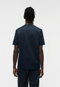 Μπλε ναυτικό κοντομάνικο T-shirt από απαλό ύφασμα. Διαθέτει στρογγυλή λαιμόκοψη και διακριτική λεπτομέρεια λογοτύπου στο πίσω μέρος κοντά στον γιακά.