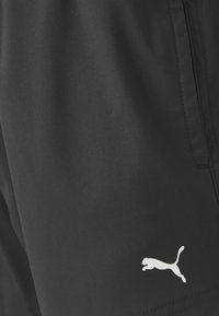Shorts noirs en tissu léger avec une texture lisse. Présente un logo Puma blanc près de l'ourlet inférieur. Design simple sans motifs.