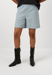 Ljusblå vävda shorts med elastisk midja, med en avslappnad passform och längd till mitten av låret, som är kombinerade med svarta cowboyboots.