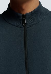 Donkerblauwe ritssweater met een geribde kraag en textuur, voorzien van een zwarte rits en minimalistische ontwerpelementen.