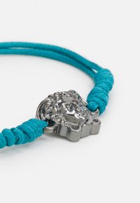 Bracelet en cuir avec cordon turquoise tressé et pendentif en métal argenté en forme de tête de Méduse. Présente un design élégant et des détails complexes.