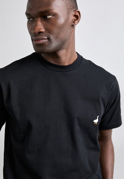 Must must T-särk, millel on ümmargune kaelus ja lühikesed varrukad, millel on vasakul küljel väikene valge tikandiga hani.