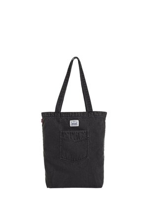 Zwarte denim draagtas met lange hengsels, voorzak en klein wit label boven de zak op een effen achtergrond.