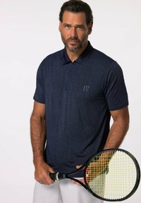Námořnické polo tričko s texturovaným vzorem, poloviční zip na límci a malé logo na levé straně. Model drží tenisovou raketu se žlutými strunami.