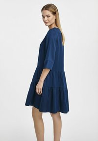 Granatowa sukienka warstwowa o luźnym kroju, z rękawami 3/4 i miękkim materiałem. Posiada okrągły dekolt i zwiewną sylwetkę.