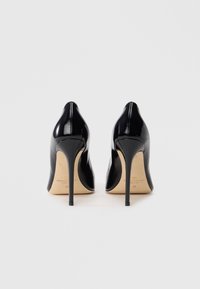 Μαύρες γόβες από δερμάτινο λακαρισμένο υλικό με μυτερή μύτη και λεπτό τακούνι στιλέτο. Λείος υφή και χρυσαφί λογότυπο στη σόλα.