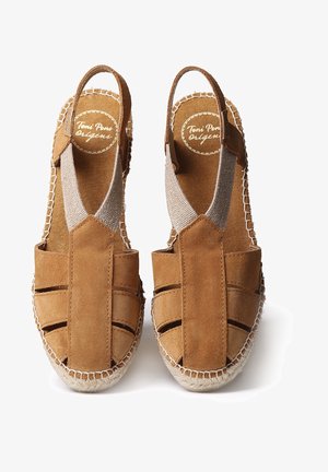 Espadrilles en daim marron avec inserts élastiques sur les côtés, semelle en jute tressé et coutures apparentes. Modèle à bout ouvert et à bride de cheville.