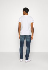 T-shirt branca de mangas curtas e decote em V, combinada com jeans de ganga azul. Os jeans têm um design clássico com cinco bolsos e um ligeiro desgaste.
