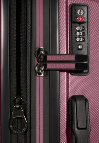 Valigia rigida di colore rosa con duplice cursore etichettato "REDOLZ", un lucchetto a combinazione integrato di colore nero e una maniglia laterale.