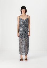 Rochie din voal cu imprimeu leopard gri, cu bretele reglabile, corp mulat și lungime maxi fluxată, asortată cu sandale negre cu curea.