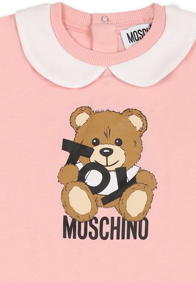 Camicia di cotone rosa con colletto bianco, decorata con un orsetto dei cartoni animati che tiene un cartello con la scritta "TOY" e il nome del brand "MOSCHINO" in brutto nero.