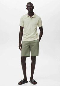 Svetle zelená polo tričko, olivově zelené šortky a černé kluzké sandály. Neformální oblečení s krátkým rukávem, slim fit a uvolněným stylem.