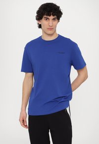 Blå bomulds t-shirt med rund hals og korte ærmer; har et lille sort logo trykt på brystet; glat tekstur.