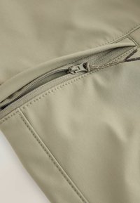 Olivzāles zaļas krāsas audums ar gludu tekstūru, kas aprīkots ar rāvējslēdzēja kabatu ar sudraba krāsas vilcēju un pastiprinātu šuvumu gar malām.