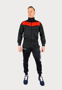 Zwart trainingspak met een rode streep op de borst, bestaande uit een ritsjack en broeken met elastische tailleband. Accentuert met het "GIVOVA" logo in het wit.