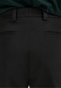 Pantaloni neri su misura con una texture liscia, un sottile intreccio diagonale, vestibilità slim e due tasche posteriori con aperture strette.