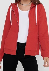 Rode zip-hoodie met een trekkoordcapuchon, twee voorzakken en contrasterende witte rits en trekkoorden. Zachte stof en een relaxte pasvorm.
