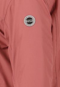Hellrosa Outdoor-Jacke mit glatter Textur, ausgestattet mit einem runden grauen Logoabzeichen auf dem Ärmel, das "ZIGZAG EXPLORING ACTIVE LIFESTYLE" liest.