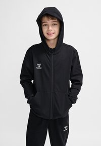 Schwarze Zip-Hoodie aus weichem Stoff mit Kapuze, ausgestattet mit vorderen Taschen und einem weißen Logo auf der linken Brust. Lässiges Design, lockere Passform.