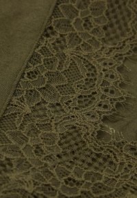 Olive green fabric with intricate lace detailing. The lace features a floral pattern and is positioned alongside a textured, solid area.