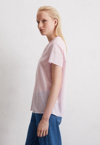 Helles rosa, kurzärmliges Baumwollhemd mit lockerer Passform und rundem Ausschnitt, kombiniert mit blauen Jeans. Glatte Textur, einfaches Design.