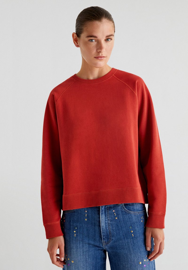 Rode sweatshirt met geribbelde ronde halslijn en lange raglanmouwen, gecombineerd met spijkerbroek met decoratieve sequins.