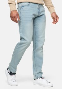Vaqueros de un azul claro, confeccionados en denim, con un corte recto, costuras visibles y cuatro bolsillos, combinados con zapatillas deportivas blancas.