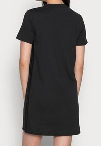 Svart kortärmad klänning i mjuk bomull, med rak skärning ochlogodetaljer längs sömmen. Slät textur, enkel design.