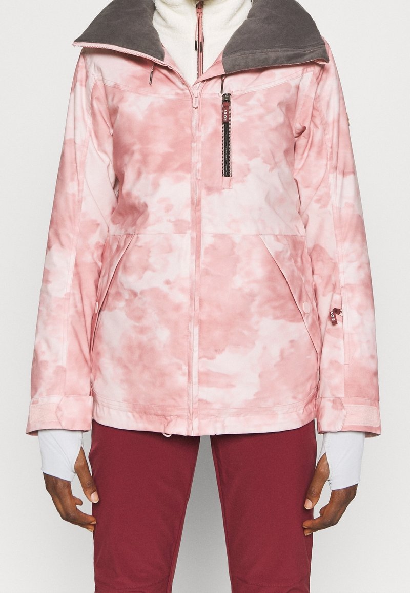 Rosa Batikjacke mit einem grauen Fleecekragen, vorderem Reißverschluss und zwei Seitentaschen. Verfügt über elastische Bündchen und atmungsaktiven Stoff.