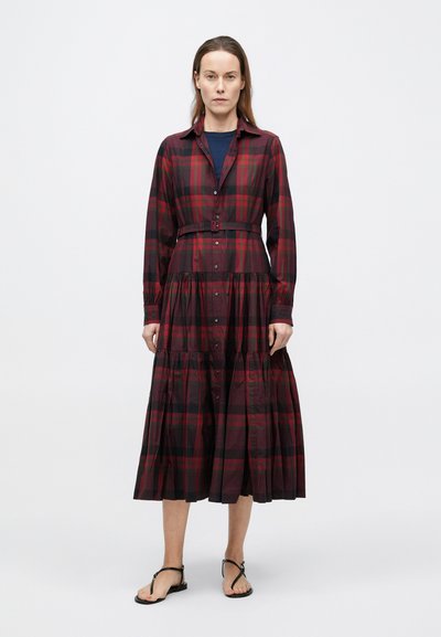 Garš, bordo krāsas rozā pledēta kleita ar pogu aizdari, apkakli un jostu viduklī. Aprīkota ar pakāpju svārku daļu un garām piedurknēm. Valkāta ar melnām sandālēm.