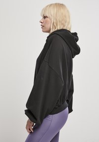 Felpa nera oversize con coulisse regolabile, caratterizzata da maniche larghe e una vestibilità rilassata, abbinata a leggings viola chiaro.