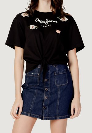 Czarna koszulka z kwiatowym haftem i logo, związana w talii, w zestawieniu ze spódnicą dżinsową z guzikami z przodu i kieszeniami.