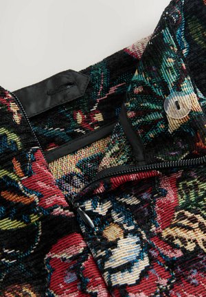 Nahaufnahme eines strukturierten Stoffes mit Blumenmuster in lebhaften Farben, einem Reißverschluss und einem Knopf nahe dem Kragen.
