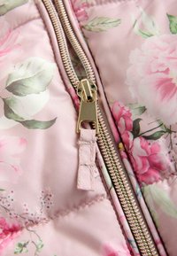 Lyserødt quiltet stof med blomsterprint og gyldent lynlåsdetalje, med store blomster og grønne blade, glat tekstur med synlige syninger.