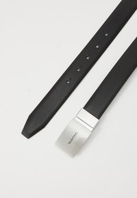 Zwart leren riem met een elegante, gestructureerde afwerking, voorzien van een zilveren rechthoekige gesp met de gravure "VALENTINO." Vijf verstelbare gaatjes.
