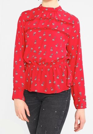 Rode blouse met lange mouwen, ronde halslijn, bloemenpatroon, geplooide taille en gerimpelde accenten; gecombineerd met donkerdenim jeans.