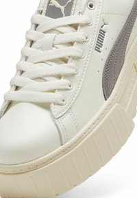 Vita lädersneaker med grå accenter, tjock plattformssula, texturerad sidopanel och platta bomullssnören. Har Puma-logotypen på tungan.