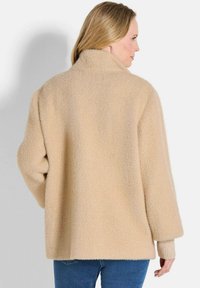 Beige, textuur wol coat met een brede kraag en verlaagde schouders. Heeft een losse pasvorm en geribbelde cuffs, ontworpen voor warmte en comfort.
