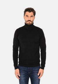 Maglione a collo alto nero realizzato in un tessuto a maglia liscia, con maniche lunghe e una silhouette aderente, abbinato a jeans blu.