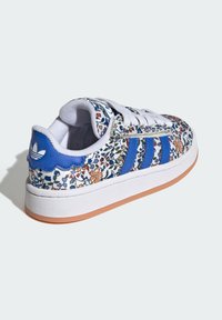White sneaker with floral patterns in blue, orange, and green, featuring three blue stripes and a textured rubber sole. Double-stitch detailing.