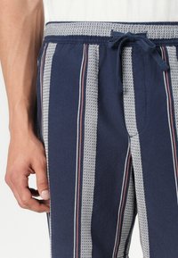 Marine gestreifte Shorts mit weißen und roten Akzenten. Verfügt über einen elastischen Bund mit Kordelzug und einem strukturierten Stoff.