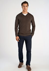 Brązowy sweter w serek, granatowe spodnie, brązowe buty żeglarskie ze sznurówkami; teksturowany materiał, dopasowany krój, styl casual.