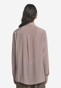 Långärmad blus i ljusrosa med vertikala ränder. Har en klassisk krage, knappmanschetter och en böjd fåll. Tillverkad av ett mjukt tyg.