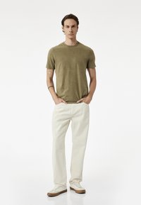 Oliwkowa, krótki rękaw koszulka noszona z jasnobeżowymi spodniami o prostym kroju i jasnymi sneakersami. Gładki materiał o luźnym kroju.