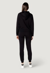 Czarna bluza z kapturem i komplet dresowy wykonane z miękkiego materiału, charakteryzujące się luźnym krojem i prążkowanymi mankietami, zestawione z białymi trampkami.