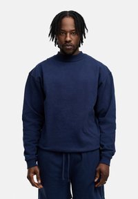 Marineblauer Baumwollpullover mit ribbeligem Rundhalsausschnitt und langen Ärmeln, der einen lässigen Schnitt und eine strukturierte Textur aufweist.